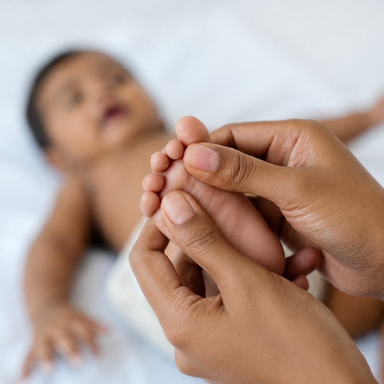 A parent's hands gently holding a baby's foot.